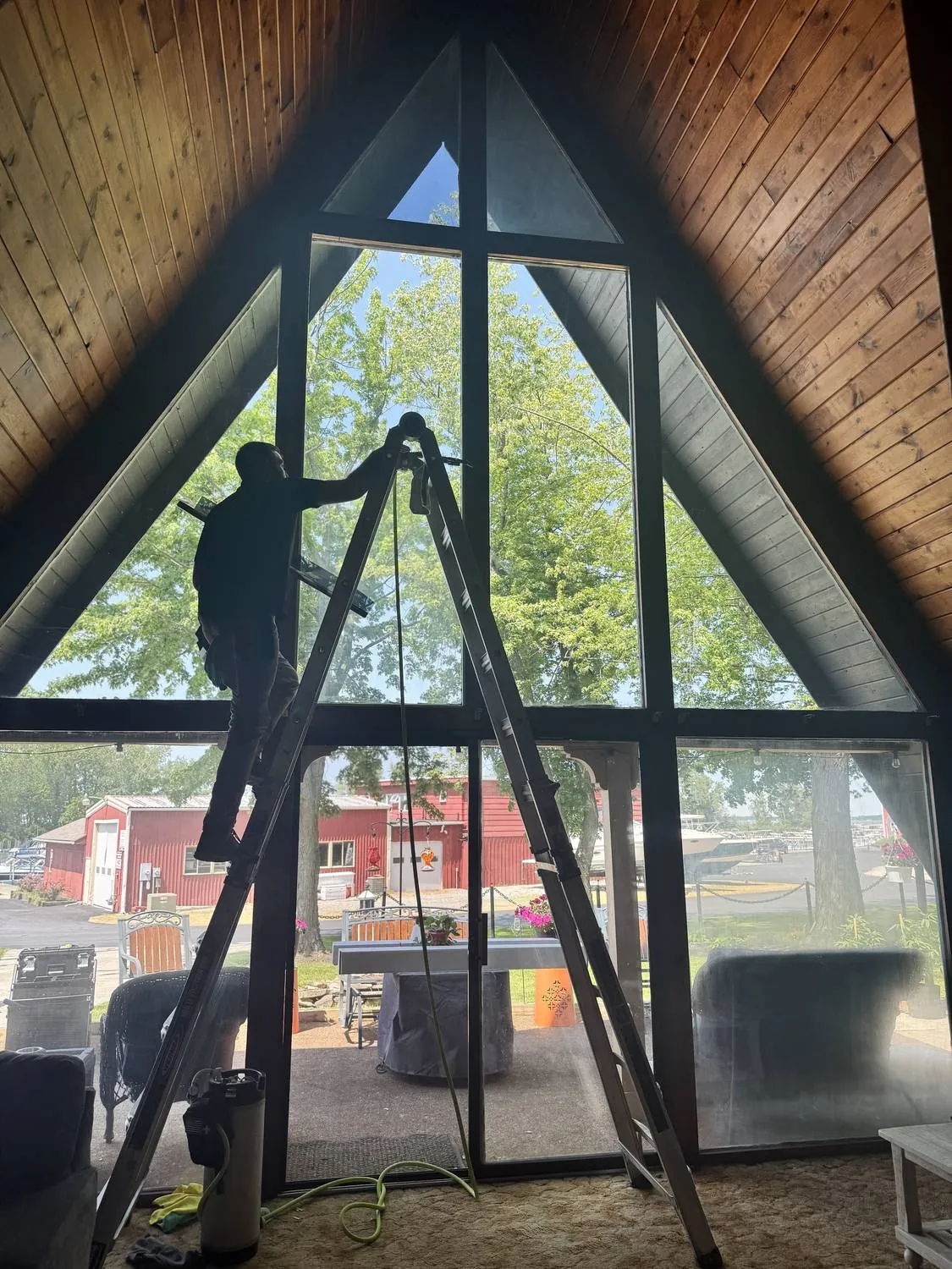 Raydiant technician installing solar window film on the tall glass wall of an A-frame lake home near Cleveland, Ohio