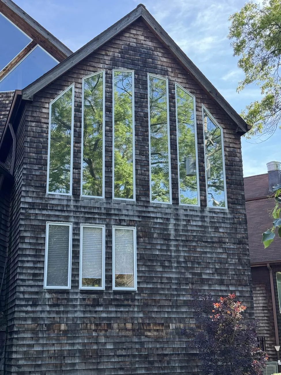 Cedar-shingle home with tall angled gable feature windows reflecting mature trees